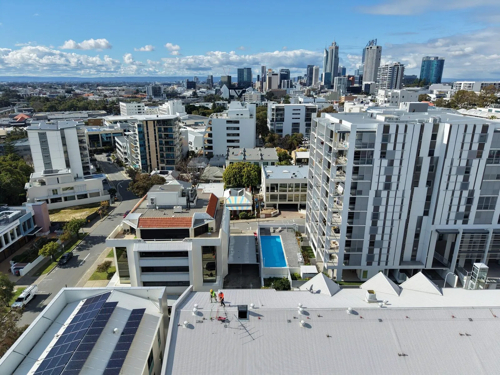 Aerial view of two inspectors on a commercial metal roof with the Perth city skyline behind